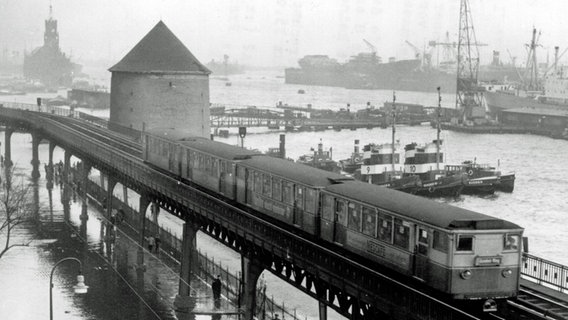 Eine U-Bahn fährt am Hamburger Hafen an einem Turmbunker vorbei (22.12.1954). Im Hintergrund ist links der alte Kaispeicher A zu sehen, wo seit 2016 die Elbphilharmonie steht. © picture-alliance / dpa 