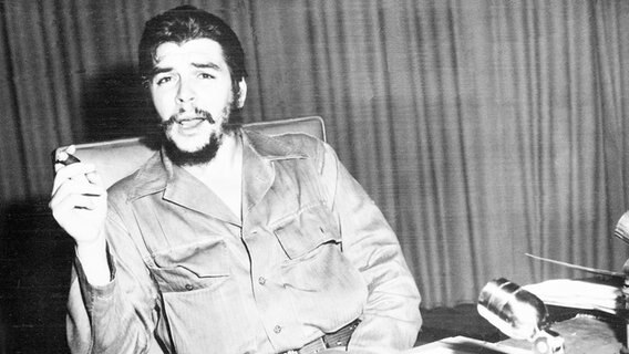 Ernesto "Che" Guevara sitzt an einem Schreibtisch. In der Hand hält er eine Havana. © picture alliance / ASSOCIATED PRESS 