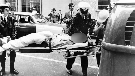 Ein Mann, der bei dem RAF-Anschlag auf das Springer-Hochhaus in Hamburg am 19.05.1972 verletzt wurde, wird in einen Krankenwagen geschoben. © picture-alliance/dpa 