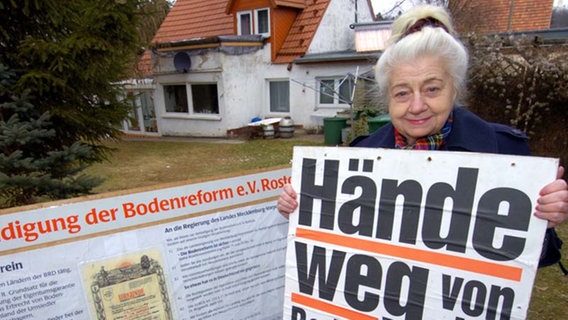 2004: Eine Rostocker Bürgerin zeigt ein Protestplakat gegen die Enteignung von Bodenreformland. © (c) ZB - Fotoreport Foto: 2004: Die Rostockerin Margot Hein zeigt ein Protestplakat gegen die Enteignung von Bodenreformland.