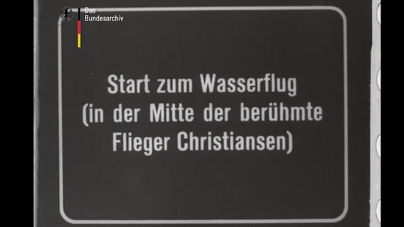 Auf einer Stummfilm-Tafel steht "Start zum Wasserflug (in der Mitte der berühmte Flieger Christiansen) Auf einer Stummfilm-Tafel steht "Start zum Wasserflug (in der Mitte der berühmte Flieger Christiansen) © Bundesarchiv Foto: Screenshot