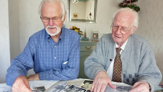 Die ehemaligen Polizisten Harald Freese (l.) und Alfred Zewuhn schauen sich Dokumente von der Sturmflut 1962 an. © NDR Foto: Petra Volquardsen