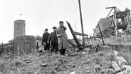 Drei Bewohner besichtigen am 1. März 1952 die völlig zerstörte Hauptstraße der Insel Helgoland © dpa picture alliance Foto: Jochen Blume