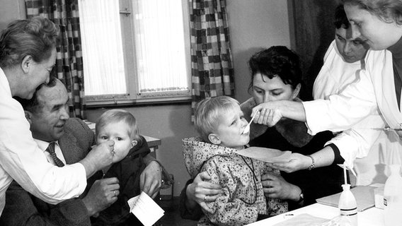 Kinder schlucken mit Impfstoff gegen Polio präparierte Zuckerwürfel, aufgenommen im November 1962 in Baden-Württemberg. © picture-alliance / dpa 