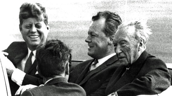 John F. Kennedy (l.) mit Berlins Regierendem Bürgermeister Willy Brandt (M.) und Bundeskanzler Konrad Adenauer in einem offenen Wagen in Berlin 1963. © picture-alliance / dpa 