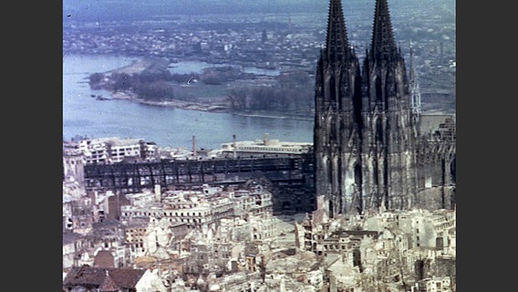Farbige Luftaufnahme von Köln: vorn Häuserruinen, dahinter der Kölner Dom und der Rhein. © dpa 