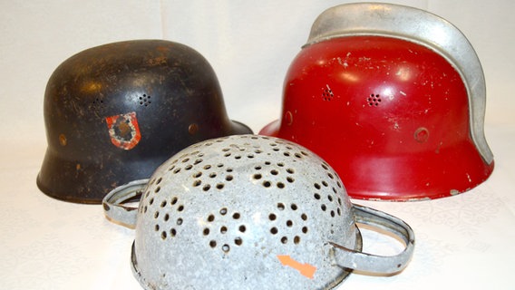 Zu sehen links ein Stahlhelm Modell 35 (= Jahr der Einführung), ein Sieb oder Durchschlag, der aus einem Stahlhelm hergestellt wurde (Mitte) sowie ein mit roter Farbe umlackierter Helm, der von der Feuerwehr genutzt wurde. © Sammlung Herbert Wintersohl 