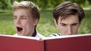 Zwei Teenager lesen im Park, einer von ihnen gähnt. © picture alliance / Cultura RF Foto: Axel Bernstorff