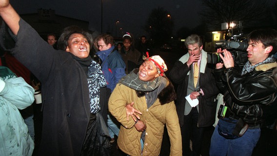 Ein Kameramann filmt zwei trauernde Afrikanerinnen nach dem Brandanschlag auf ein Asylbewerberheim in der Lübecker Hafenstraße im Januar 1996. © picture-alliance / dpa Foto: Rolf Rick