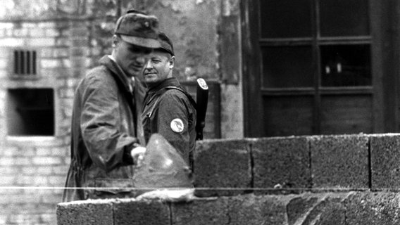 Ein Bauarbeiter errichtet am 18. August 1961 unter der Aufsicht eines Volkspolizisten an der Sektorengrenze am Potsdamer Platz eine mannshohe Mauer. © picture-alliance / dpa Foto: Bratke