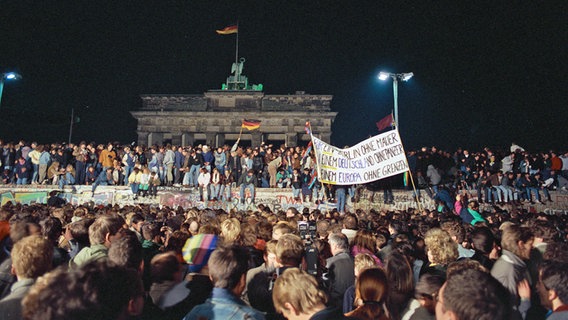Einen Tag nach der Grenzöffnung in Berlin feiern Tausende Menschen auf der Berliner Mauer am Brandenburger Tor. © dpa-Report Foto: Peter Zimmermann