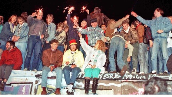 Menschen sitzen am 10. November 1989 auf der Berliner Mauer und feiern © dpa Foto: DB