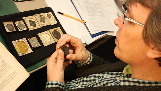 Dr. Ralf Wiechmann schaut sich im Museum für Hamburgische Geschichte 300 Jahre alte Medaillen an, die sich mit dem Pestausbruch 1712 in Hamburg befassen. © NDR Foto: Oliver Diedrich