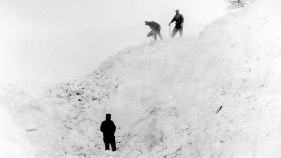 Männer stehen inmitten der meterhohen Schneeberge auf Rügen im Winter 1979. © NDR Foto: Marlies Schumacher