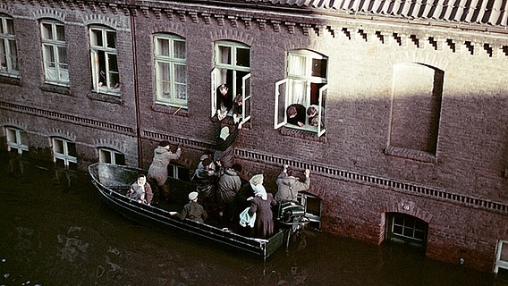 Helfer retten ein Kind per Boot aus einem eingeschlossenen Wohnhaus im überschwemmten Hamburg-Wilhelmsburg 1962 © NDR Foto: Hildegard Westphal