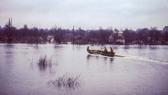 Drei Menschen in Rettungswesten auf einem Boot im überschwemmten Hamburger Stadtgebiet nach der Sturmflut im Februar 1962. © NDR Foto: Karl-Heinz Pump