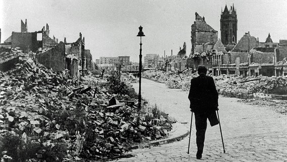 Ein beinamputierter Kriegsversehrter humpelt nach dem Zweiten Weltkrieg durch das zerstörte Hamburg. © dpa 