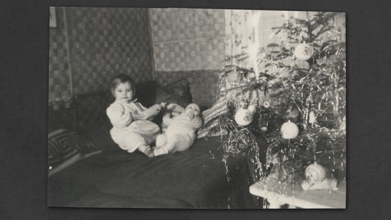 Ein Baby sitzt neben einem Christbaum in einer so genannten Nissenwohnung. © Stiftung Freilichtmuseum am Kiekeberg Foto: Privat