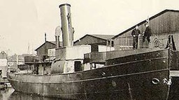 Die MS Skagerrak, ein kleiner Dampfer mit großem Schornstein, liegt am Pier.  