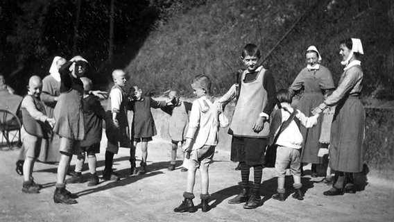 Geistig behinderte Kinder spielen mit zwei Diakonieschwestern um 1930 Ringelreihen © dpa - Report 