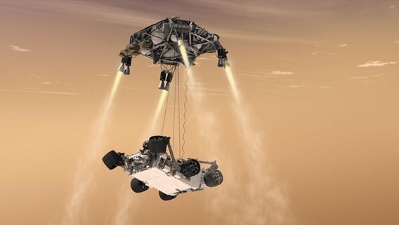 Eine Illustration zeigt, wie der Marsrover Curiosity unter anderem mithilfe eines sogenannten Skycrane auf den Mars abgelassen wird. © NASA/JPL-Caltech 
