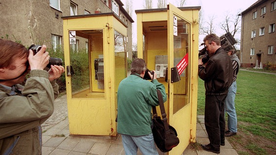 Journalisten inspizieren am 22. April 1994 eine Telefonzelle in Berlin Treptow, in der am Morgen der Kaufhaus-Erpresser "Dagobert" von Spezialkräften festgenommen wurde. © picture alliance / AP Foto: Jockel Finck
