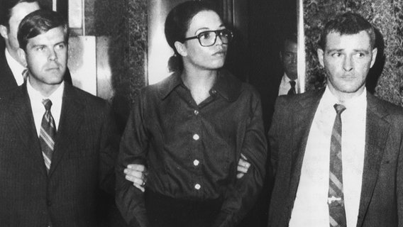 Die Bürgerrechtlerin Angela Davis wird am 13. Oktober 1970 in Handschellen von zwei FBI-Beamten beim Verlassen des FBI-Hauptquartiers in New York eskortiert. Die Bürgerrechtlerin Angela Davis wird am 13. Oktober 1970 in Handschellen von zwei FBI-Beamten beim Verlassen des FBI-Hauptquartiers in New York eskortiert. © picture alliance / UPI