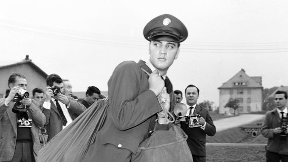 Pressefotorgrafen nehmen Elvis Presley am 2. Oktober 1958 bei seiner Ankunft in der US-Militärkaserne in Friedberg in Empfang. Der "King of Rock 'n' Roll" war einen Tag zuvor in Bremerhaven von Bord gegangen. © picture alliance / AP | STR 