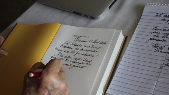 Eine weibliche Hand schreibt mit einem Füller eine Widmung in ein aufgeschlagenes Buch. © Anne Siegel 