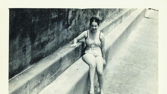 Eine Frau sitzt in einem Badeanzug auf einer Mauer und lächelt in die Kamera. © Anne Siegel 