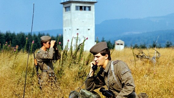 Zwei Soldaten der DDR-Grenztruppen des Grenzkommandos Süd vor einem Wach- und Beobachtungsturm kontrollieren einen Abschnitt der innerdeutschen Grenze am Brocken, aufgenommen im Juni 1987. © picture-alliance/ ZB Foto: Hans Wiedl