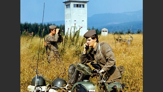 Zwei Soldaten der DDR-Grenztruppen des Grenzkommandos Süd vor einem Wach- und Beobachtungsturm kontrollieren einen Abschnitt der innerdeutschen Grenze am Brocken, aufgenommen im Juni 1987. © picture-alliance/ ZB Foto: Hans Wiedl