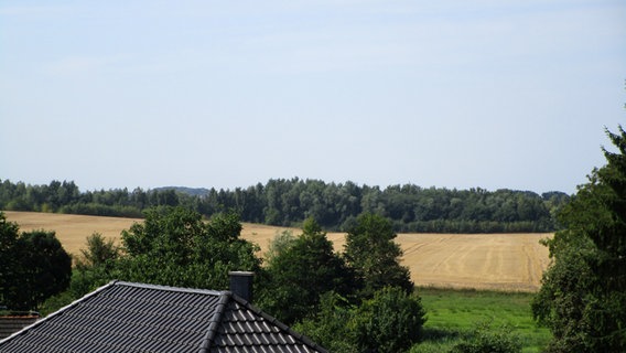 Ein Hausdach, dahinter ein Feld und ein Waldstück © NDR Foto: Axel Seitz