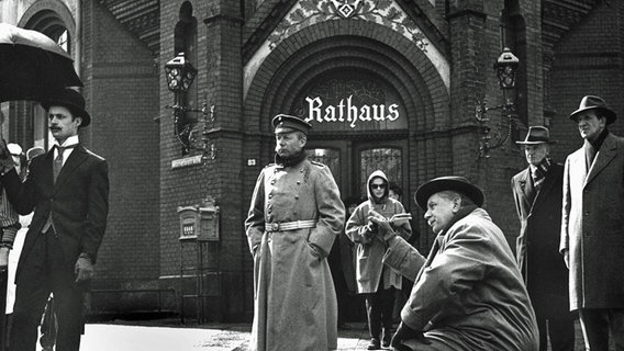 Regisseur Helmut Käutner (hockend, rechts) gibt letzte Anweisungen für eine Aufnahme des Films "Der Hauptmann von Köpenick" mit Heinz Rühmann (Mitte). © dpa - Bildarchiv 