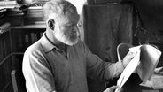 Schriftsteller Ernest Hemingway (1899 - 1961) liest an seinem Schreibtisch in einem Manuskript, undatierte Aufnahme. © picture alliance / ZUMAPRESS.com | KEYSTONE Pictures USA 