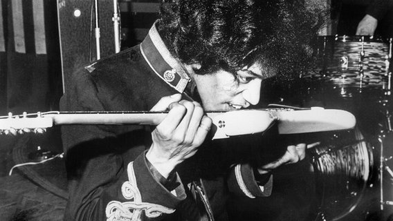 Der US-amerikanische Rocksänger und Gitarrist Jimi Hendrix spielt seine elektrische Gitarre während eines Konzertes mit seiner Band "Jimi Hendrix Experience" in Großbritannien 1967 mit Zunge und Zähnen. © picture-alliance / dpa | UPI 