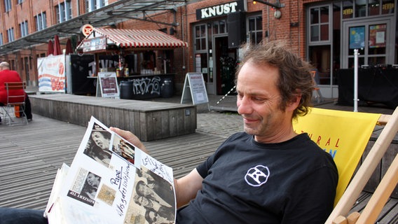 Betreiber Karsten Schölermann sitzt mit einem Fotoalbum vor dem Musikclub Knust in Hamburg. © NDR Foto: Heiko Block