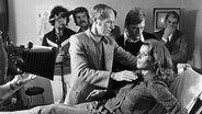 Der Naturheilpraktiker Manfred Köhnlechner hilft der Schauspielerin Senta Berger 1975 während einer Behandlung mit Akupunktur-Nadeln beim Aufrichten. © picture-alliance / dpa Foto: Horst Werner