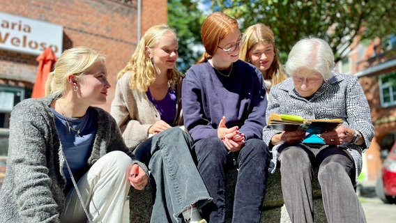 Irene Butter blickt mit vier Mädchen in ein Poesielalbum. © NDR / John Bidwell Foto: John Bidwell