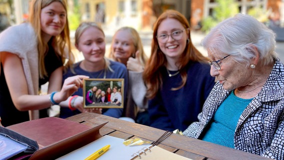 Vier Mädchen halten ein Erinnerungsfoto mit Irene Butter hoch. © NDR / John Bidwell Foto: John Bidwell