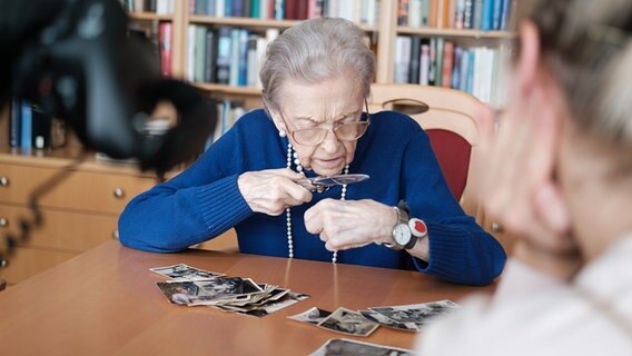 Ingrid Haerder aus Wedel sichtet mit einer Lupe alte Fotos. © NDR Foto: André Bacher