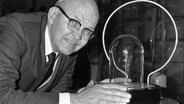 Jack Kilby posiert 1958 mit dem ersten integrierten Schaltkreis der Welt, der von einer Glasabdeckung umgeben ist. © picture alliance / AP Foto: I. INOUE