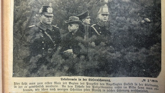 Ein historischer Zeitungsausschnitt mit einem Foto von Adolf Seefeld und Polizisten bei einer Ortsbegehung in einer Kiefernschonung. © Stadtarchiv Schwerin 