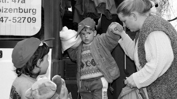 Eine Frau hilft einem kleinen Jungen aus dem Kosovo 1999 aus dem Bus zum Erstaufnahmelager Horst bei Boizenburg. © dpa/picture-alliance Foto: Bernd Wüstneck