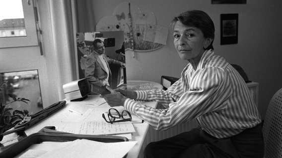 Die ehemalige Fernsehansagerin Irene Koss sitzt an einem Schreibtisch, auf dem ein Foto ihres verstorbenen Ehemannes Sammy Drechsler steht. © picture-alliance / dpa Foto: Istvan Bajzat