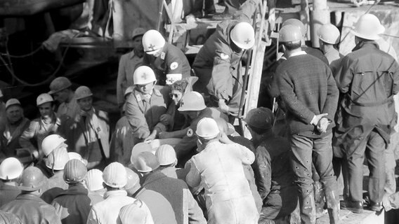 Sanitäter tragen am 7.11.1963 nach dem Bergwerksunglück im niedersächsischen Lengede einen der elf geretteten Bergleute ins Freie. Er trägt eine Sonnenbrille als Schutz vor dem grellen Licht. © picture-alliance Foto: Sven Simon