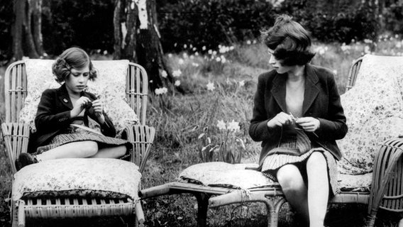 Prinzessin Elizabeth (rechts), die spätere Queen, und ihre Schwester Prinzessin Margaret sitzen 1940 im Garten von Schloss Windsor und stricken für britische Soldaten, die im zweiten Weltkrieg kämpfen. © dpa- Bildarchiv 