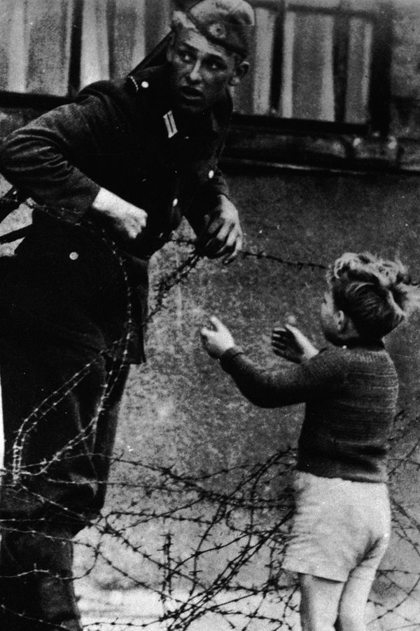 Ein kleiner Junge will Mitte August 1961 über die Sektorengrenze. Ein DDR-Grenzsoldat hilft ihm dabei. © picture-alliance / akg-images 