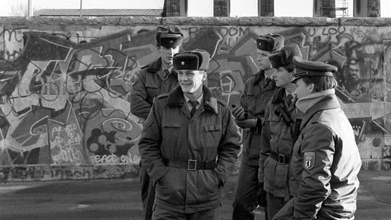 Angehörige der DDR-Volkspolizei (l.) unterhalten sich am 7. Dezember 1989 an der Mauer vor dem Brandenburger Tor mit einem West-Berliner Polizisten (r). © dpa - Bildarchiv Foto: DB Kneffel