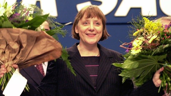 Nach ihrer Wahl zur neuen Vorsitzenden der CDU bedankt sich Angela Merkel bei den Delegierten des CDU-Bundesparteitages in Essen und winkt mit zwei Blumensträußen. © picture-alliance/dpa Foto: Michael Jung